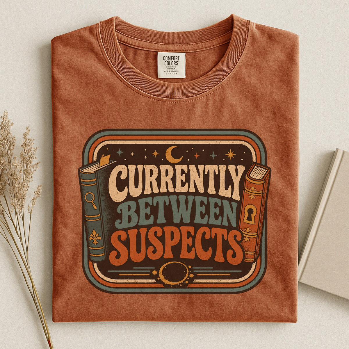 Shelf Love Studio Currently Between Suspects t-shirt in Yam, styled flat lay