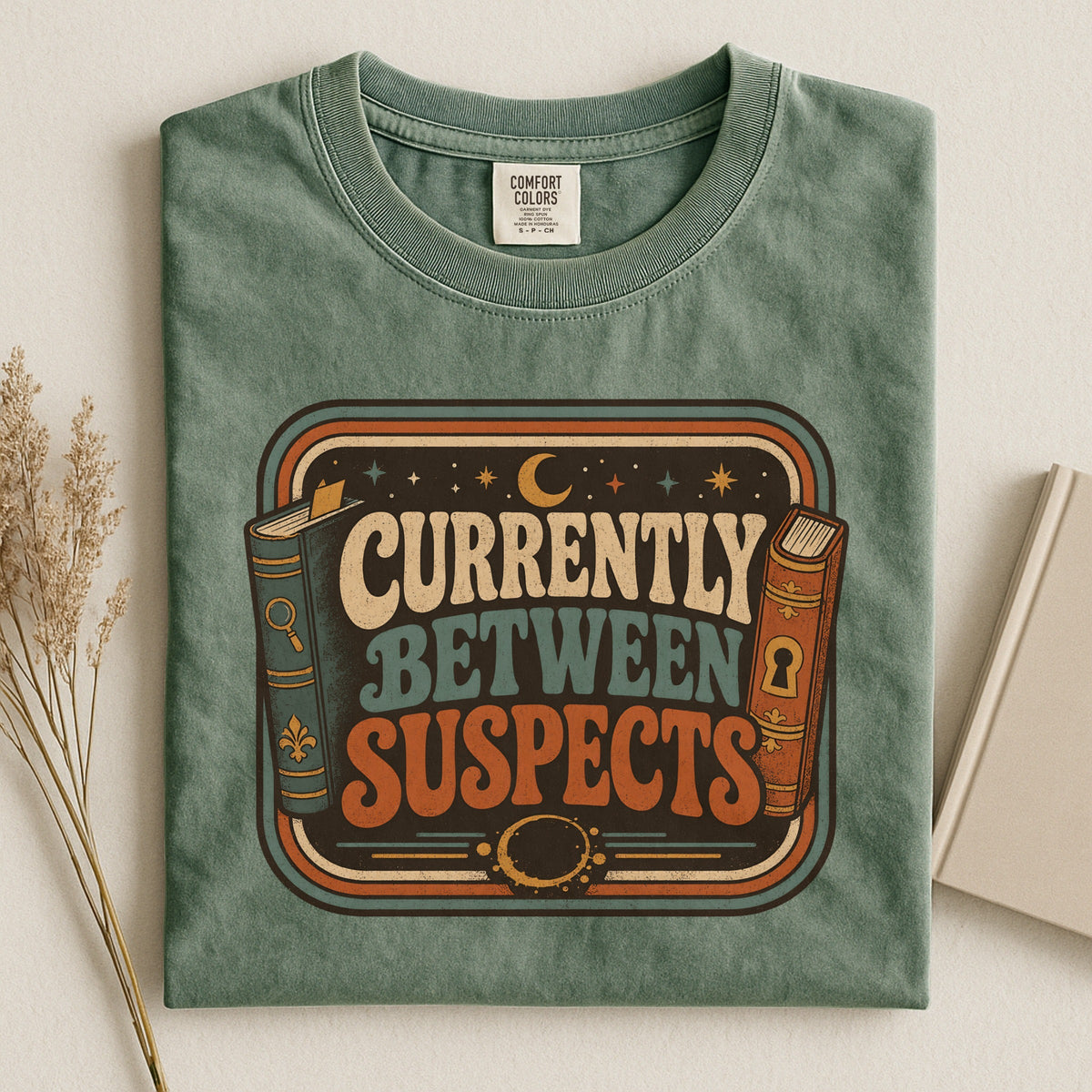 Shelf Love Studio Currently Between Suspects t-shirt in Moss, styled flat lay