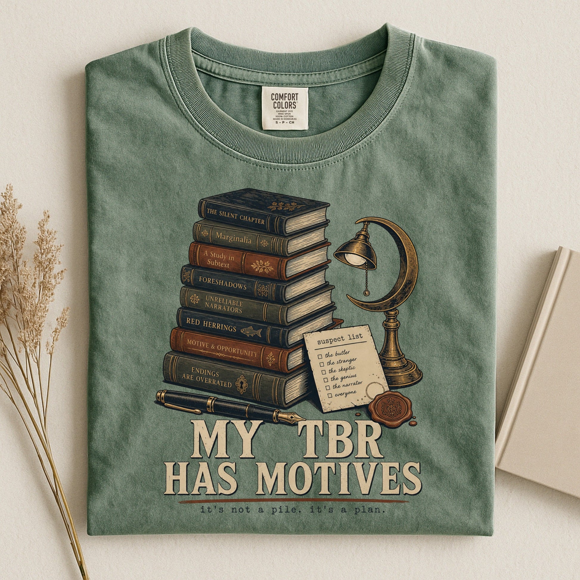 My TBR Has Motives bookish tee in Moss, flat lay